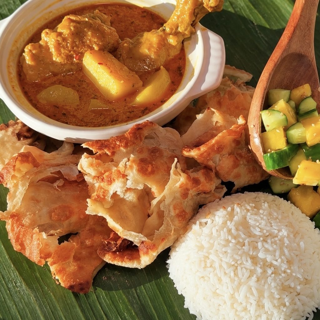 Roti canai with curry, rice and cucumber pickle on banana leaf